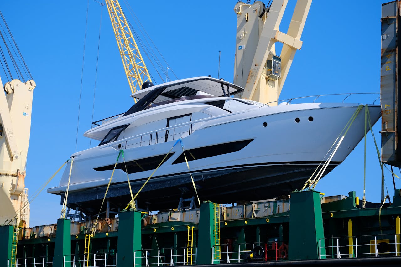 A gleaming white yacht being lifted by a crane, set against a clear blue sky during the day.