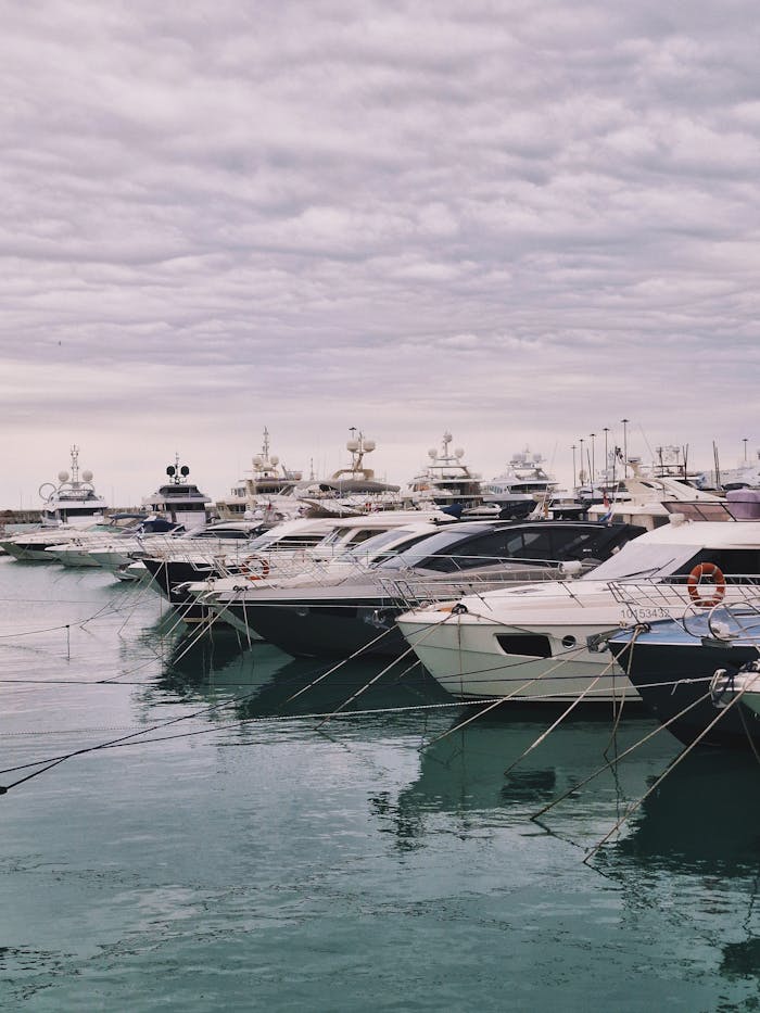 A row of luxurious yachts docked at a serene marina under a cloudy sky.